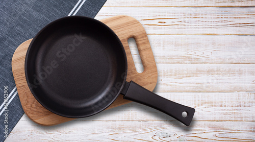 Photo Black fry pan and board with napkin on wooden table