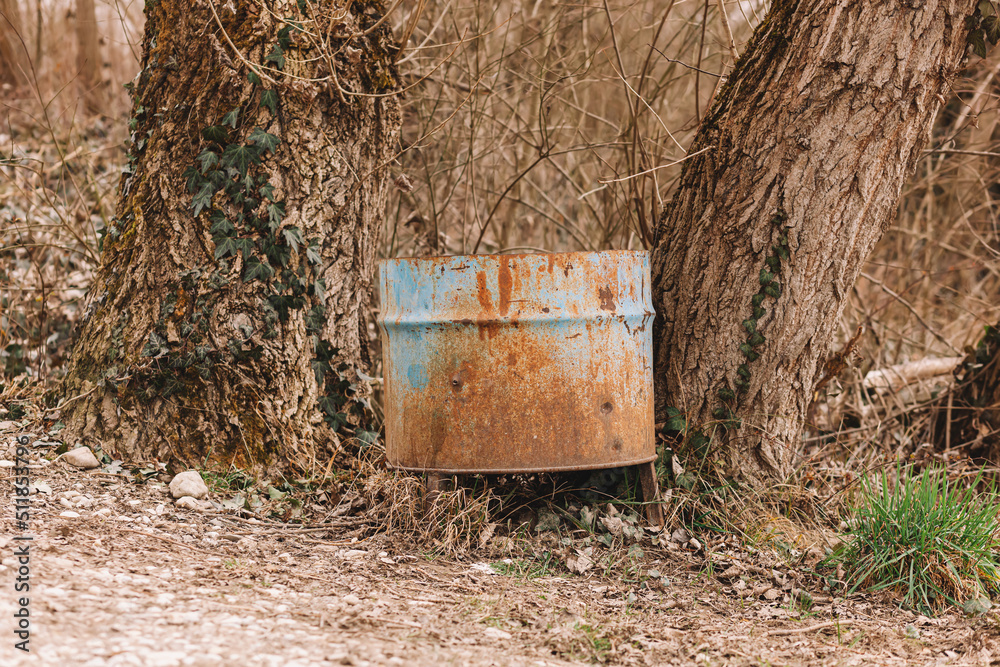 Blue metal steel rusty trash can under the trees on the forest trail Blue metal steel rusty trash can under the trees on the forest trail
