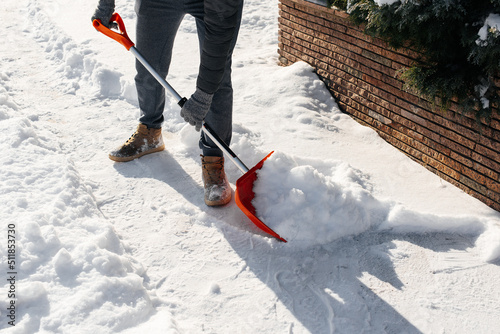 Close-up of a man cleaning and clearing snow in front of the house on a sunny and frosty day. Cleaning the street from snow on a winter day. Snowfall, and a severe snowstorm in winter.