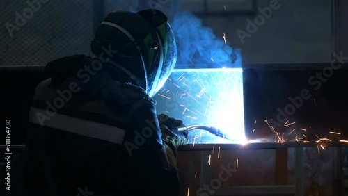 Welder welds large trailer frame at a factory. Employee of a factory for welding parts is actively working to pass the shift.