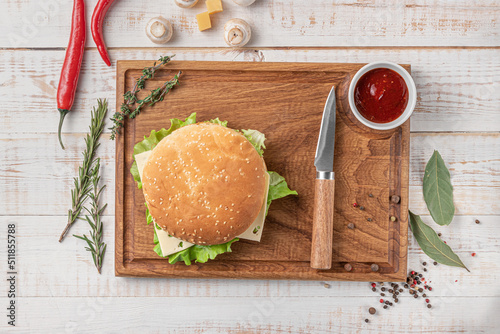 square wooden cutting board of dark color with edging. burger with salad and cutlet, mushrooms, chili pepper and spices on a white background, top view