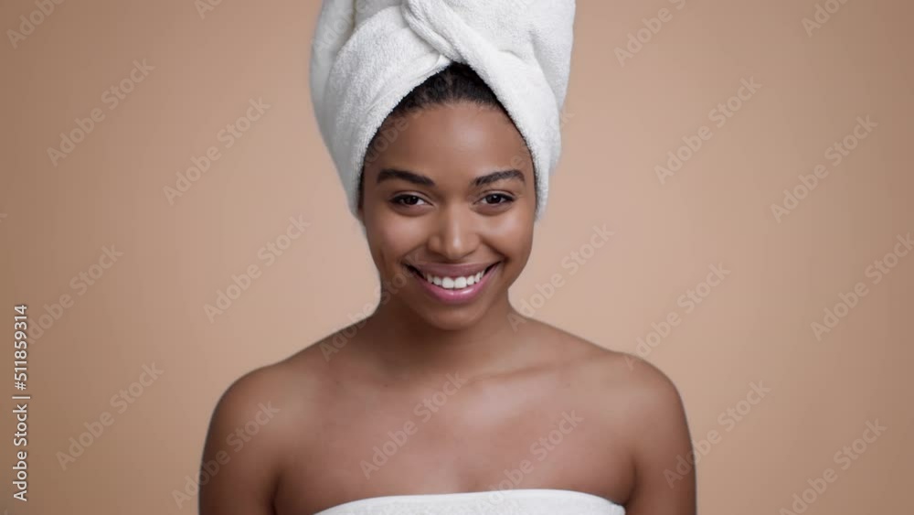 Studio portrait of young beautiful african american woman with towel on head smiling to camera, beige background Studio portrait of young beautiful african american woman with towel on head smiling to camera, beige background