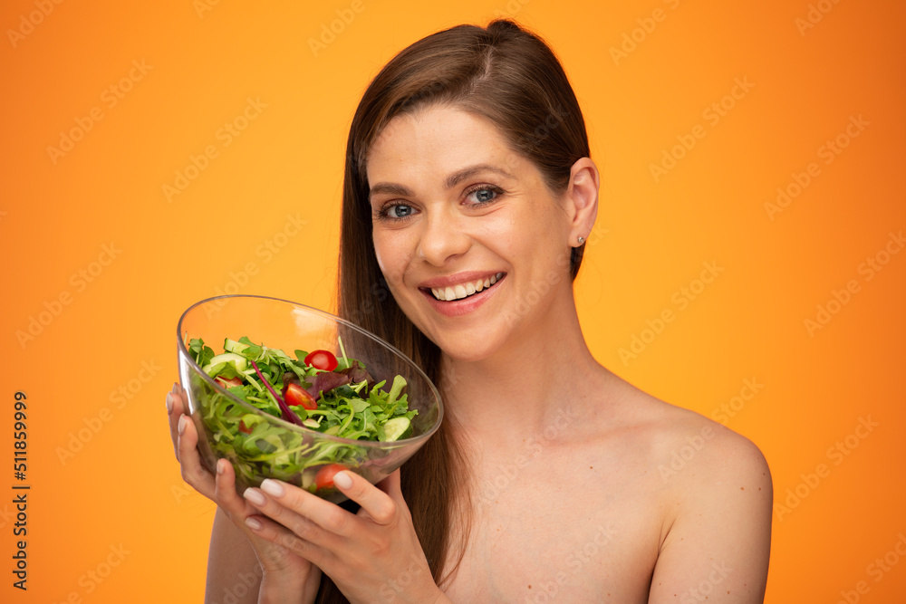 Woman holding green salad. Smiling girl with bare shoulders isolated portrait on orange yellow background. Woman holding green salad. Smiling girl with bare shoulders isolated portrait on orange yellow background.