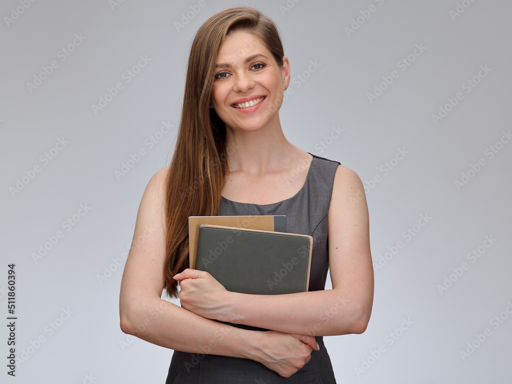 Smiling teacher or student woman in gray business dress holding books in front of her, isolated portrait. Smiling teacher or student woman in gray business dress holding books in front of her, isolated portrait.