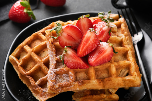 Belgium waffles. Homemade waffles with strawberries, powdered sugar and cup of coffee on black plate on black stone table background. Breakfast. Top view. Mockup for design idea.