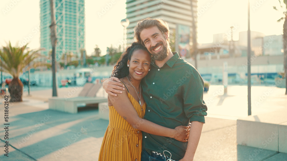 © Andrii Nekrasov - Close-up portrait of happy interracial couple in the port, backlighting Closeup, young woman and man hugging and smiling looking at the camera