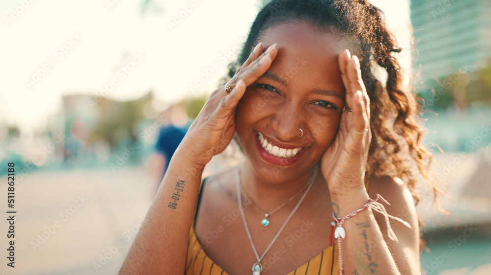 Closeup portrait of smiling woman with long curly hair on urban city background. Frontal close-up of happy girl fixing her hair and looking at the camera Closeup portrait of smiling woman with long curly hair on urban city background. Frontal close-up of happy girl fixing her hair and looking at the camera
