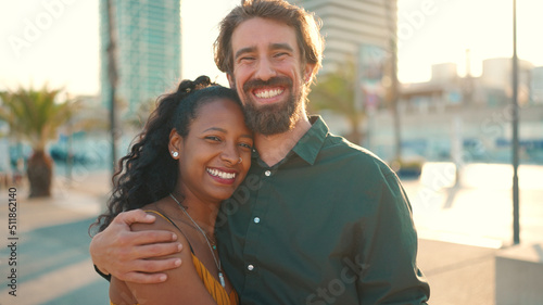 Close-up portrait of happy interracial couple in the port, backlighting Closeup, young woman and man hugging and smiling looking at the camera