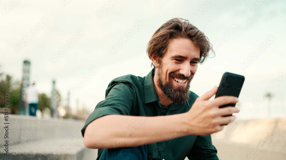 Close-up portrait of a man with a beard recording a voice message on the embankment background. Closeup of a young hipster male using a mobile phone