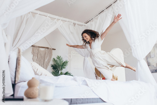 Woman joyfully jumps onto the bed with her arms outstretched as if in flight