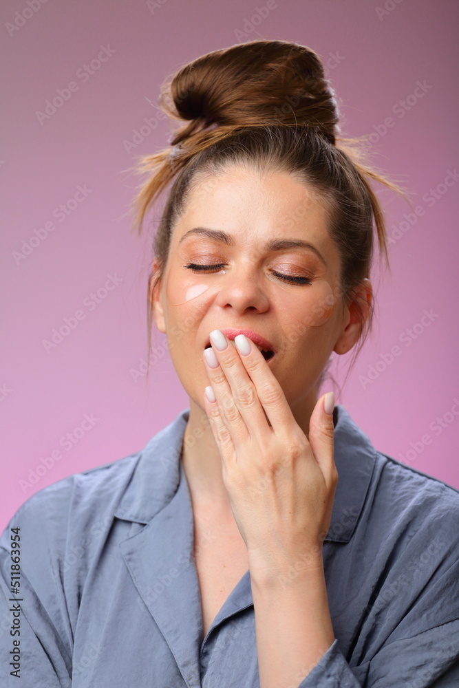Yawning woman in pajama with bun hair, isolated on pink female face portrait with under eyes patches. Yawning woman in pajama with bun hair, isolated on pink female face portrait with under eyes patches.