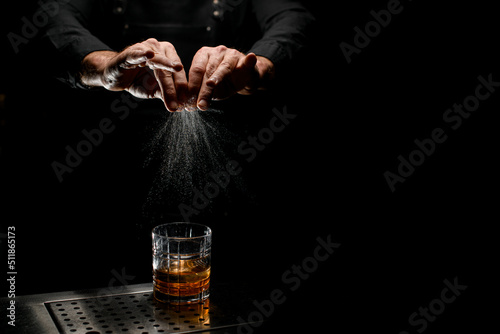 hands of bartender expressing oils from an orange peel for cocktail on dark background.