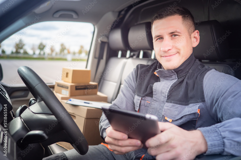 logistic delivery of something. Courier is engaged in logistic delivery. Courier driving minivan. Postman in gray uniform. Parcel cardboard boxes behind postman. Courier smiling looking at camera logistic delivery of something. Courier is engaged in logistic delivery. Courier driving minivan. Postman in gray uniform. Parcel cardboard boxes behind postman. Courier smiling looking at camera