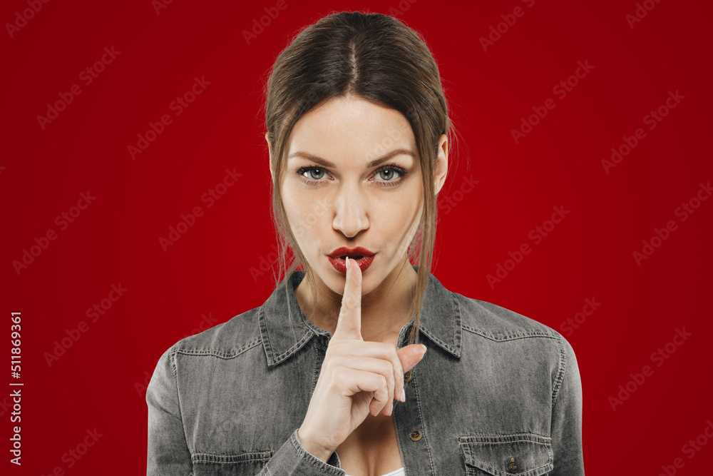 Pretty tricky female with red lips matching with color of background showing shh sign Pretty tricky female with red lips matching with color of background showing shh sign