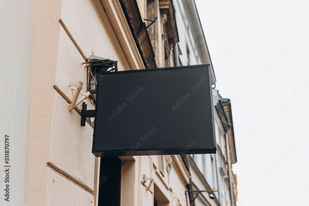 Blank sign mockup in the urban environment. Black rectangle sign with blank space for cafe or restaurant name and logo, in an old town