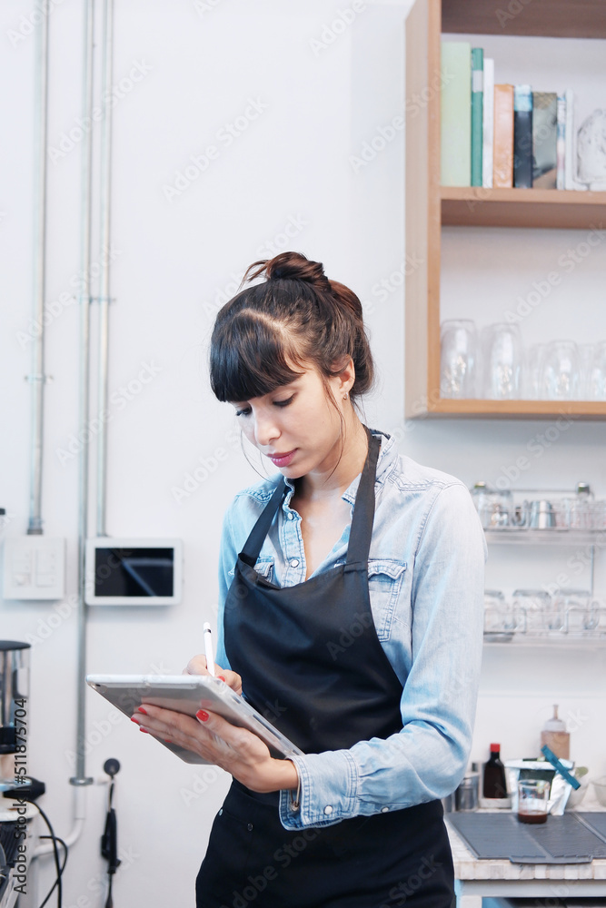 Smiling Caucasian Young barista woman is wearing apron and writing online order and menu of customers on tablet in cafe and coffee shop. Start up small cafe business and technology Concept. Smiling Caucasian Young barista woman is wearing apron and writing online order and menu of customers on tablet in cafe and coffee shop. Start up small cafe business and technology Concept.
