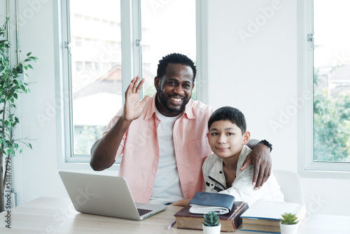 Young African teacher or tutor is teaching knowledge for Caucasian student boy and waving hello people in classroom. Education and Technology for homeschool Concept.