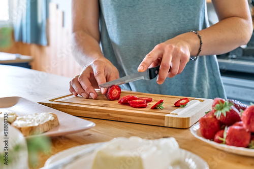 Woman making summer strawberry sandwich. Female hands cutting ripe red strawberry on cutting board. Healthy eating  fruit dieting brunch.