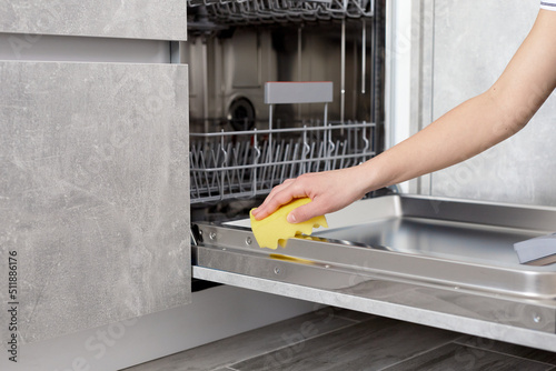 Woman hands cleaning dishwasher panel with yellow rag in kitchen. Close up. photo