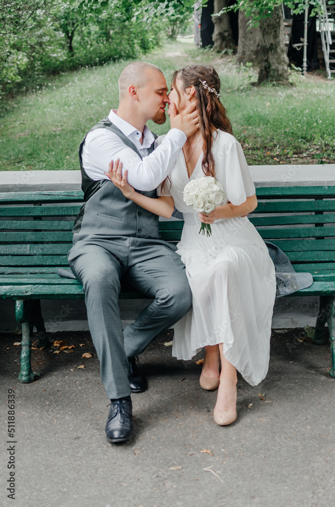 the bride and groom with a wedding bouquet kissing on a bench the bride and groom with a wedding bouquet kissing on a bench