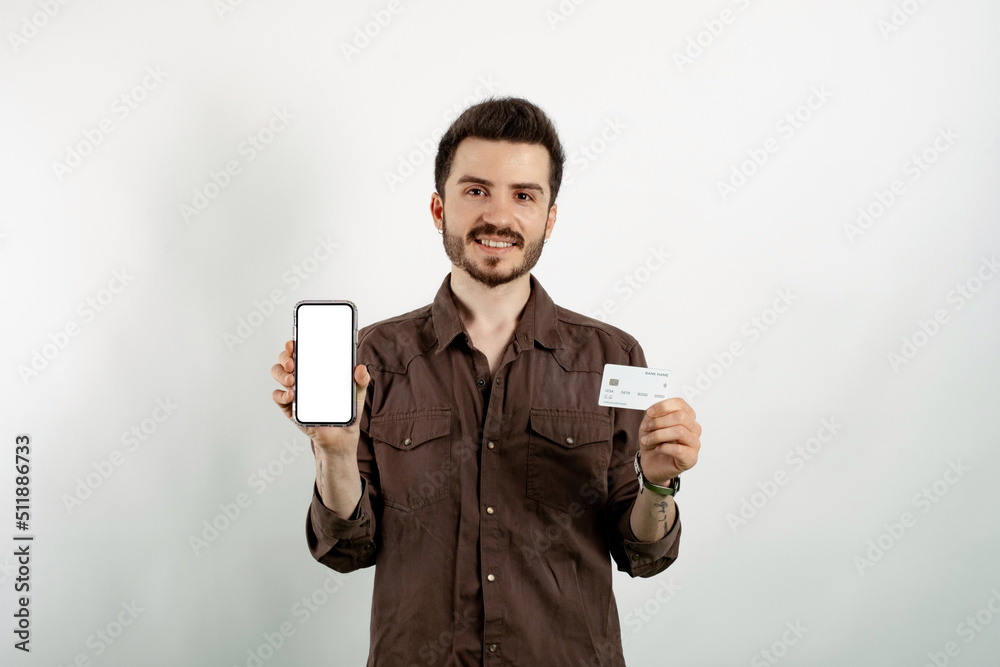 Handsome young man wearing casual clothes posing isolated over white background blank screen and credit card, recommending newest mobile app for shopping or online payment, banking, mockup. Handsome young man wearing casual clothes posing isolated over white background blank screen and credit card, recommending newest mobile app for shopping or online payment, banking, mockup.