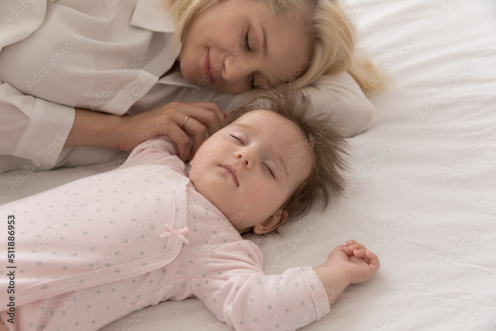 Close up above shot serene mother sleeping with infant daughter lying together on bed. Adorable babygirl looks carefree rest with loving mommy take healthy day nap at home. Maternity, babyhood concept Close up above shot serene mother sleeping with infant daughter lying together on bed. Adorable babygirl looks carefree rest with loving mommy take healthy day nap at home. Maternity, babyhood concept