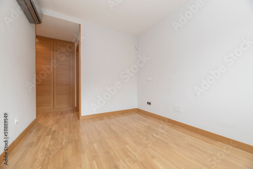 Empty room with built in oak wardrobe, gray air conditioner and light oak floor