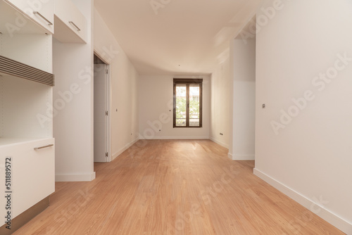 Empty apartment with light wood flooring, long window in the background and plain white painted walls