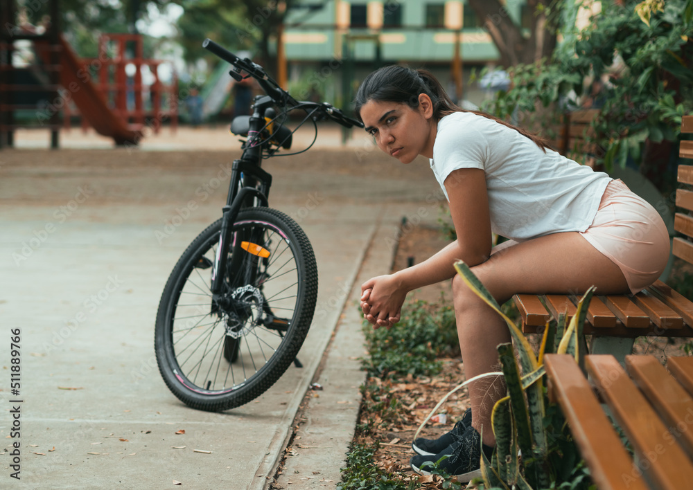 Naklejka premium latina girl sitting after cycling on a bench thinking seriously with her hands clasped together