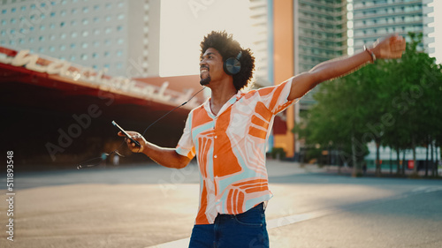 Foto Close-up of cheerful young African American man wearing shirt listening to music in headphones and dancing on urban city background