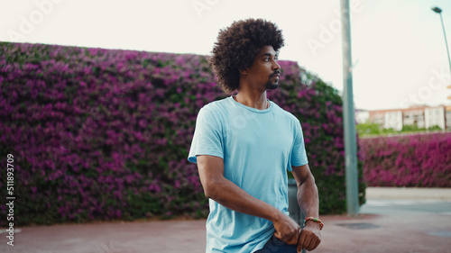 young African American man going on city street on background wall covered with purple flowers. Lifestyle concept