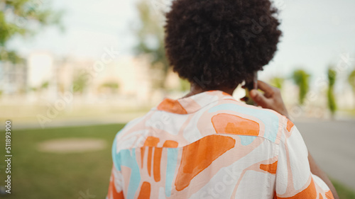 Close-up of young African American man wearing shirt walking and talking on smartphone on path in the park. Man emotionally talking on mobile phone. Lifestyle concept.