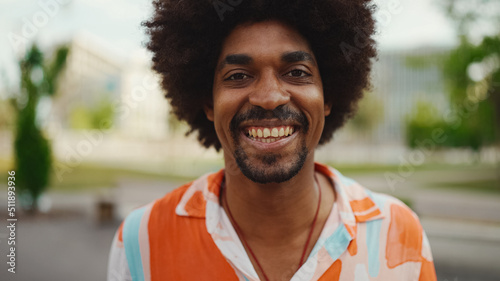 Close-up frontal portrait of young African American man wearing shirt looking at the camera and smiling. Camera moving forwards approaching the person. Lifestyle concept. © Andrii Nekrasov