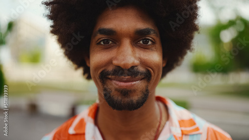 Close-up frontal portrait of young African American man wearing shirt looking at the camera and smiling. Camera moving forwards approaching the person. Lifestyle concept. © Andrii Nekrasov