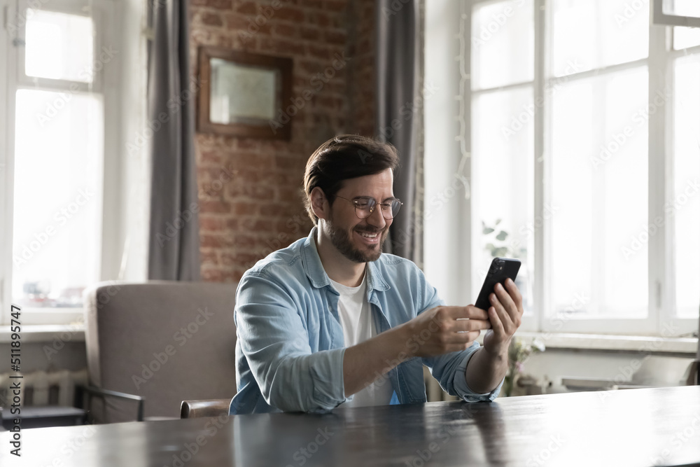 Handsome businessman sit at desk in loft home office using modern smartphone read sms with good, pleasant news, web surfing internet, spend leisure on-line. Tech, business application usage concept Handsome businessman sit at desk in loft home office using modern smartphone read sms with good, pleasant news, web surfing internet, spend leisure on-line. Tech, business application usage concept