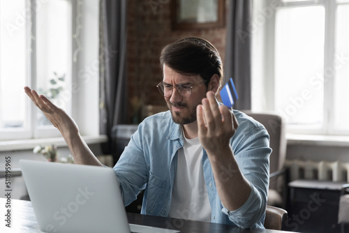 Man sit at desk with laptop use online banking service, faced with blocked credit card, financial problem, check balance feels irritated. Internet fraud, unsuccessful pay, money theft, funds overspend