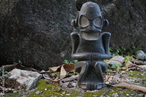 Fototapeta Taino Antique Stone Cemi Idol Figure sitting on the ground on top of moss