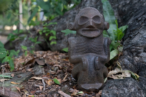 Photo Taino Antique Stone Cemi Idol Figure sitting on the ground next to dry leaves