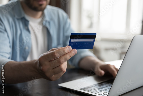 Close up view male hand holding credit card using laptop make on-line payments via e-bank application, do remote e-shopping at home. Secure e-payment, e-commerce client, instant money transfer concept