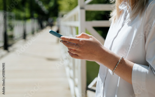 Side view of unrecognizable woman typing, browsing internet online on mobile phone on sunny day outdoors. Female hands holding smartphone, selective focus