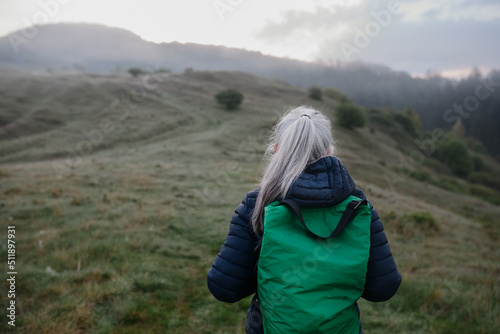 Rear view of senior woman hiking in nature on early morning with fog and mountains in background.