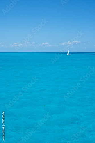 A sailboat on the horizon in the crystal clear tropical sea against the blue sky of a summer day. Travel vacations