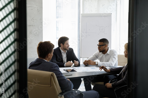 Team of serious multiracial businesspeople negotiating, solve business, search solution, seated at desk gathered in modern office boardroom. Teamwork, partnership, formal group meeting event concept