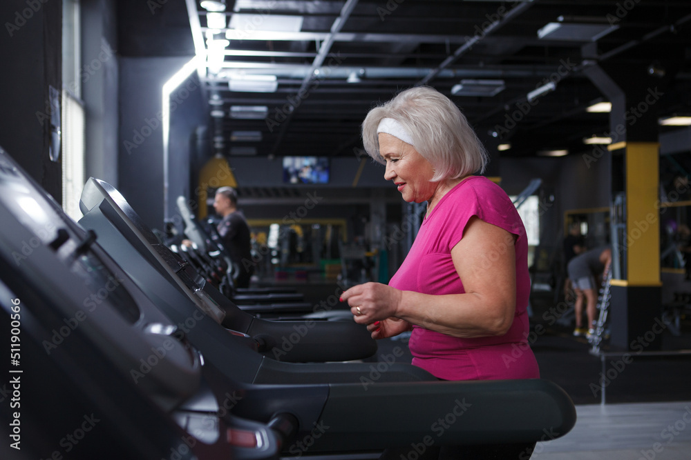 Fototapeta premium Happy healthy senior woman running on a treadmill at the gym