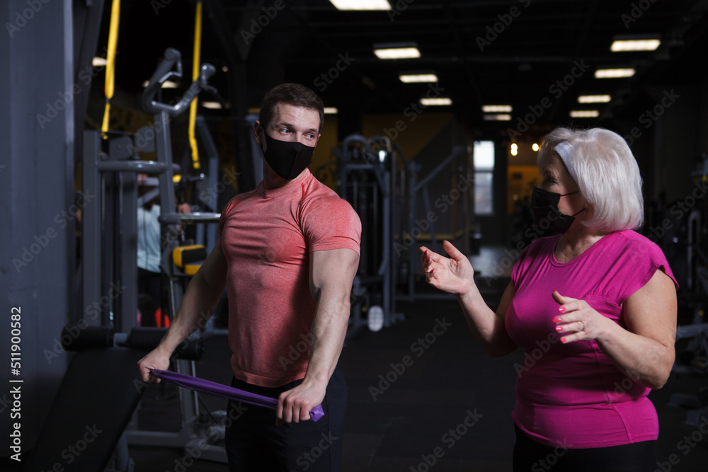 Personal trainer and his senior female client wearing medical face masks during gym workout