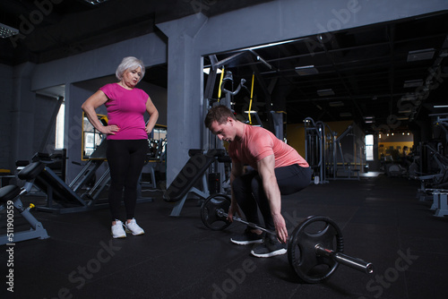 Athletic personal trainer showing his senior client how to lift barbell at the gym © mad_production
