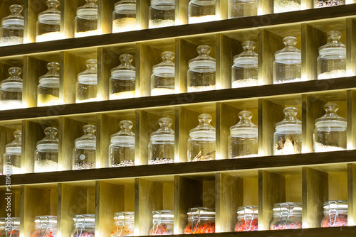 Tea and various spices in glass jars on shelves with lighting. Sale of tea in the store