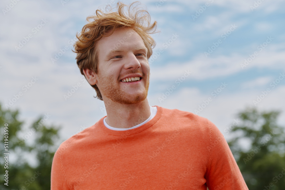Cheerful young red hair man looking away and smiling while standing outdoors Cheerful young red hair man looking away and smiling while standing outdoors