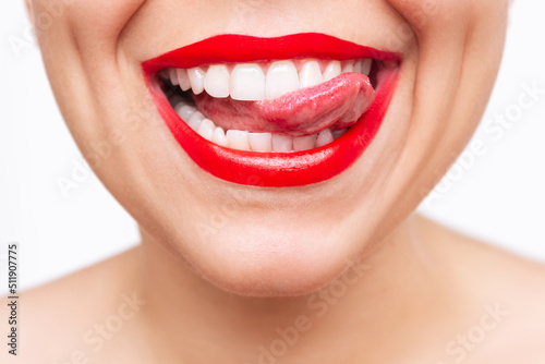 Cropped shot of young caucasian woman showing tongue and demonstrating the even teeth isolated on a white background. Perfect smile with red lipstick. Teeth whitening. Oral hygiene, dental health care