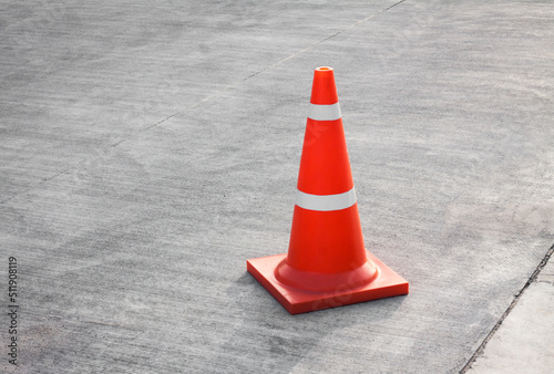 Striped orange cones on the asphalt road. Plastic orange cone on the road. Traffic cone on a parking lot in the park. traffic cone, with white and orange stripes on gray asphalt, copy space.